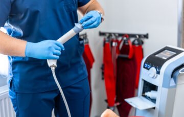 Médico gastroenterólogo con guantes quirúrgicos sosteniendo equipo de endoscopia digestiva junto a máquina especializada en clínica de Cartagena