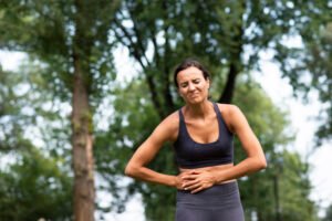 Mujer joven con ropa deportiva sujetándose el abdomen derecho con gesto de dolor, síntoma frecuente del hígado graso en etapas avanzadas